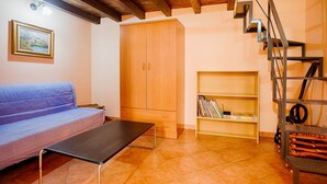 Una habitación con techo de madera, un sofá, un armario, una estantería y una escalera de metal.