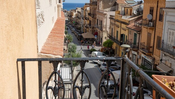 Vista callejera con edificios, cielo despejado y una lejana vista al mar.