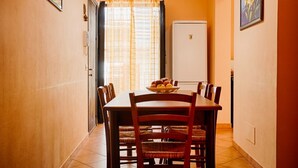 Un comedor con una mesa preparada para cuatro personas, un refrigerador al fondo y una puerta que da a otra habitación.