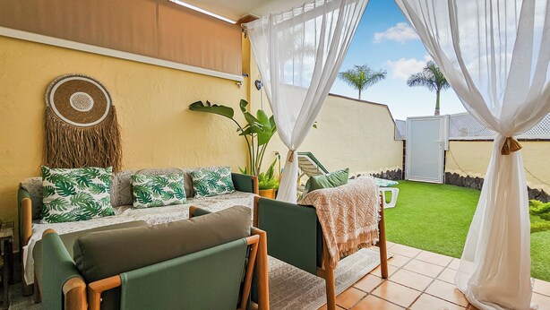 A patio area with a sofa, chairs, and a dining table. There is a wall-mounted decorative item and a potted plant.
