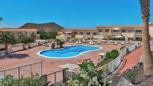 A resort with a swimming pool, palm trees, and a mountainous backdrop.