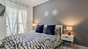 A bedroom with a bed, two bedside tables, a TV mounted on the wall, and decorative wall art.