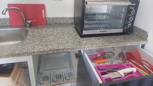 Una cucina con un tostapane, un tagliere rosso, un lavello e un cassetto pieno di utensili da cucina.