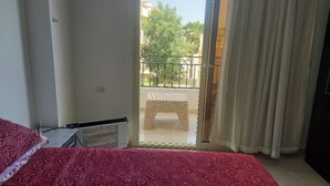 Una camera d'albergo con un letto, un termosifone, una finestra con vista su un balcone e una tenda.