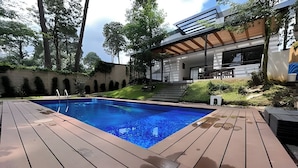 A swimming pool with a wooden deck, surrounded by a landscaped garden and a modern house with a covered patio. - Deluxe home at the heart of Avandaro (Valle de Bravo)