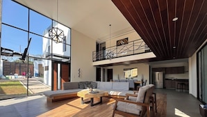 A spacious living area with a large sofa, a round coffee table, and a dining table. There is a kitchen area with modern appliances and a balcony with a railing. - Deluxe home at the heart of Avandaro (Valle de Bravo)