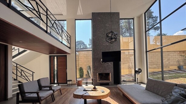 A spacious living room with a large sofa, a coffee table, and a fireplace. There is a staircase leading to an upper level. - Deluxe home at the heart of Avandaro (Valle de Bravo)
