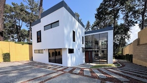 A modern two-story building with large windows and a flat roof, surrounded by trees and a paved driveway. - Deluxe home at the heart of Avandaro (Valle de Bravo)