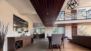 A spacious living area with a wooden dining table and chairs, a built-in kitchen, and a large window overlooking the outdoors. - Deluxe home at the heart of Avandaro (Valle de Bravo)