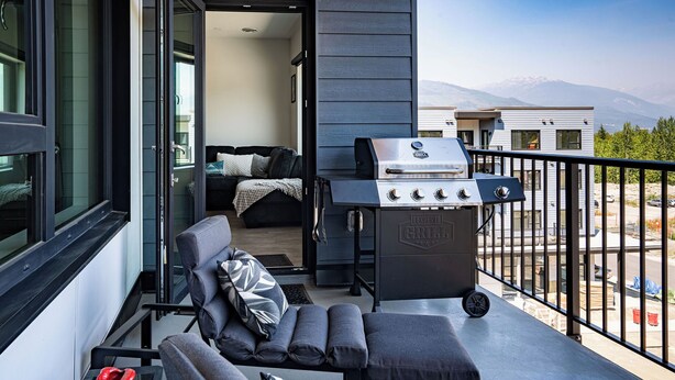 A balcony with a grill, seating area, and a view of the mountains. - Slopes and Green by Revelstoke Vacations (Revelstoke)