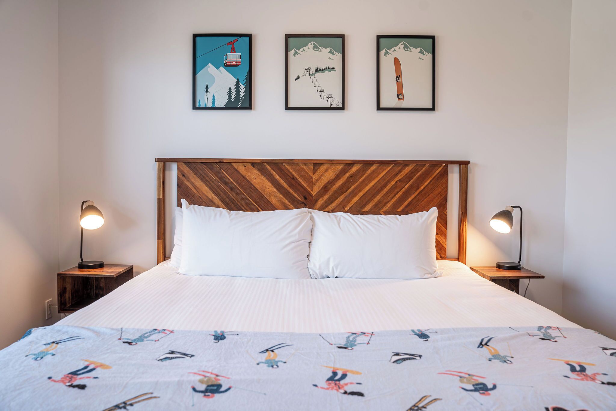 A bed with a wooden headboard, white bedding, and a colorful quilt. There are three framed pictures on the wall above the bed.