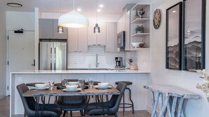 A modern kitchen with a central island, stainless steel appliances, and a dining area with a wooden table and chairs. - Slopes and Green by Revelstoke Vacations (Revelstoke)