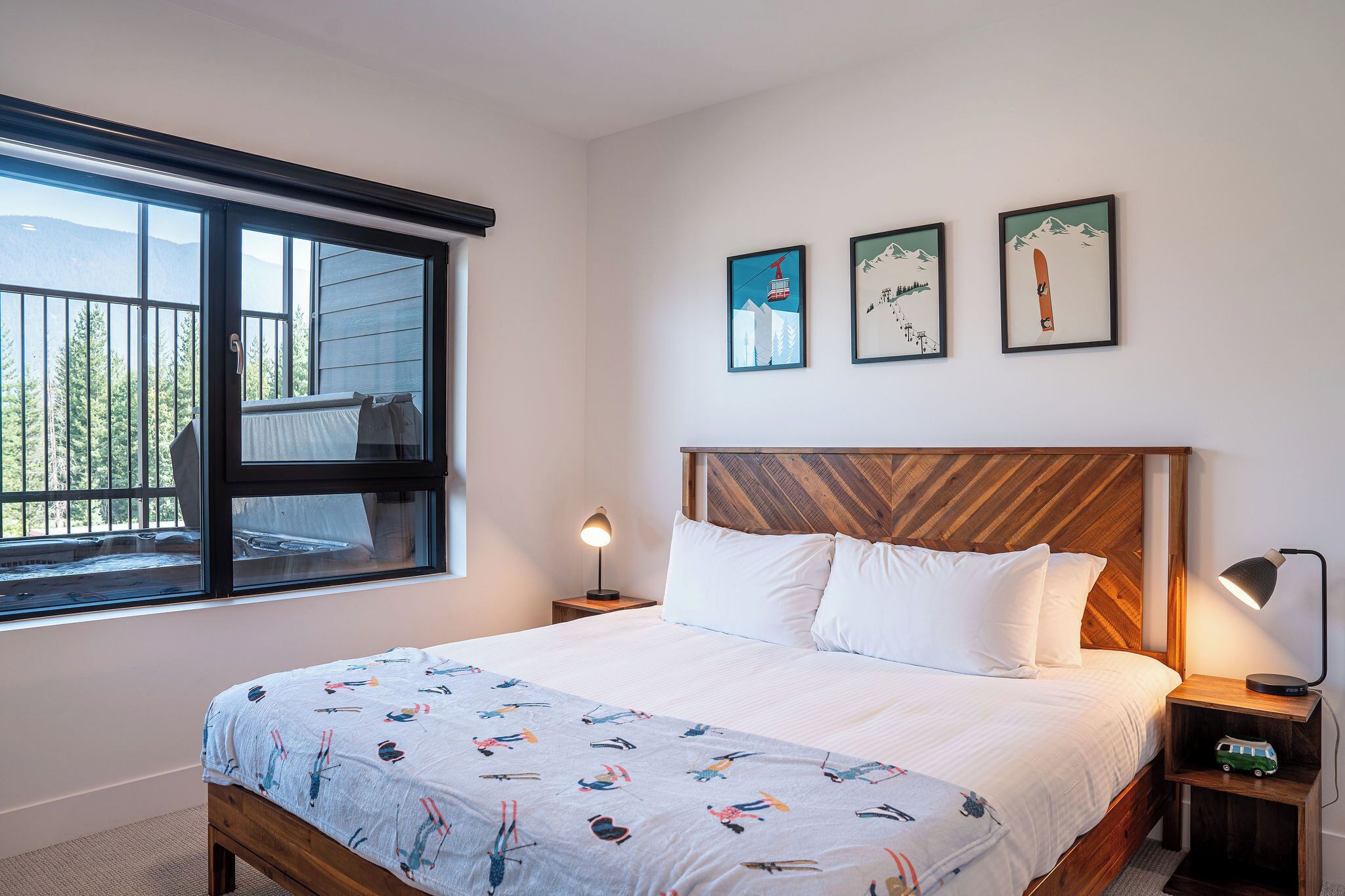 Een slaapkamer met een groot bed, een houten hoofdbord, een nachtkastje met een lamp en een raam met uitzicht op bomen en bergen.