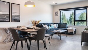 A modern living room with a dining area, large windows with a mountain view, and artwork on the walls. - Slopes and Green by Revelstoke Vacations (Revelstoke)