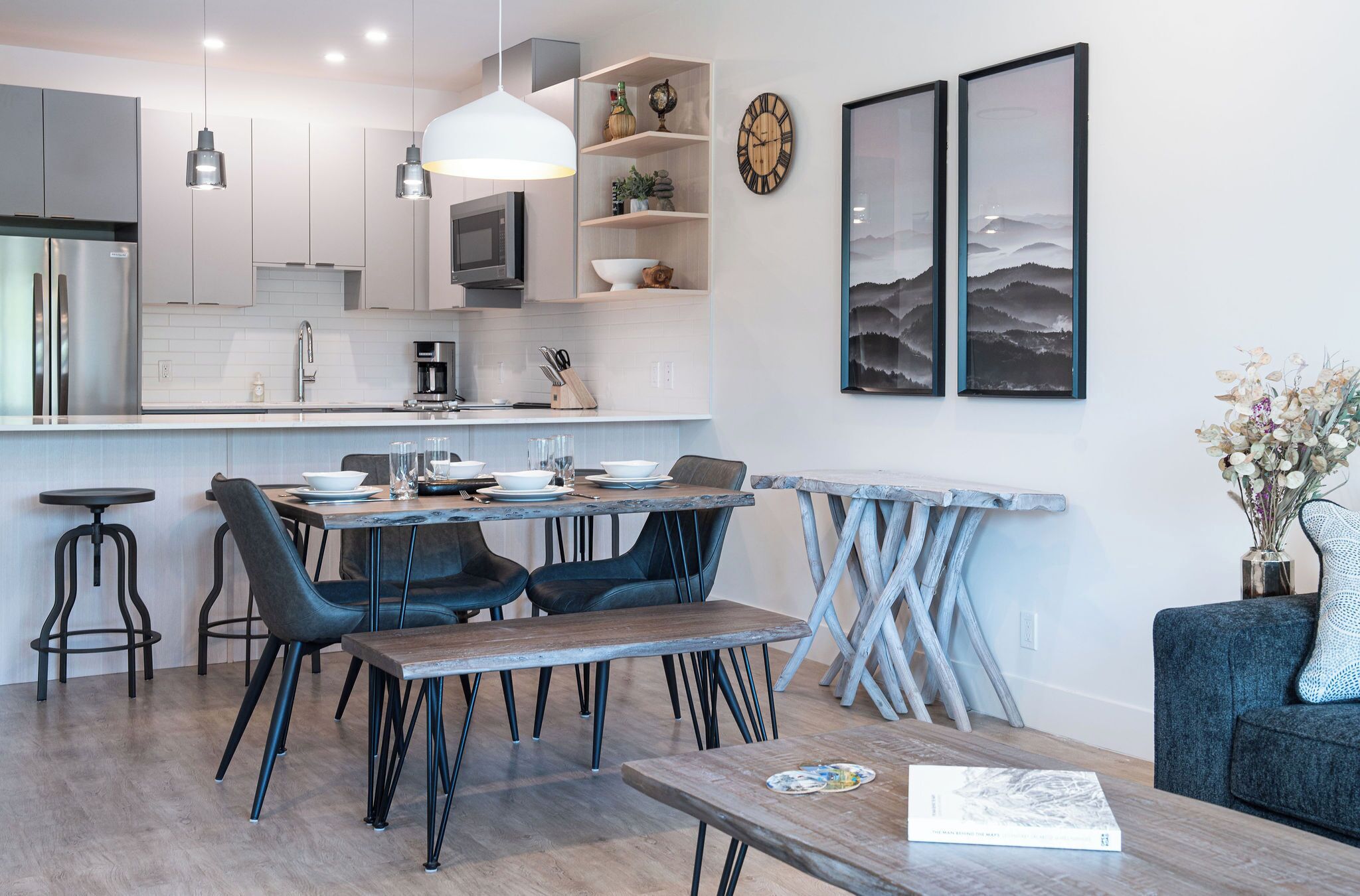 Une cuisine moderne avec des meubles blancs, un réfrigérateur en acier inoxydable et un coin repas comprenant une table et des chaises en bois.