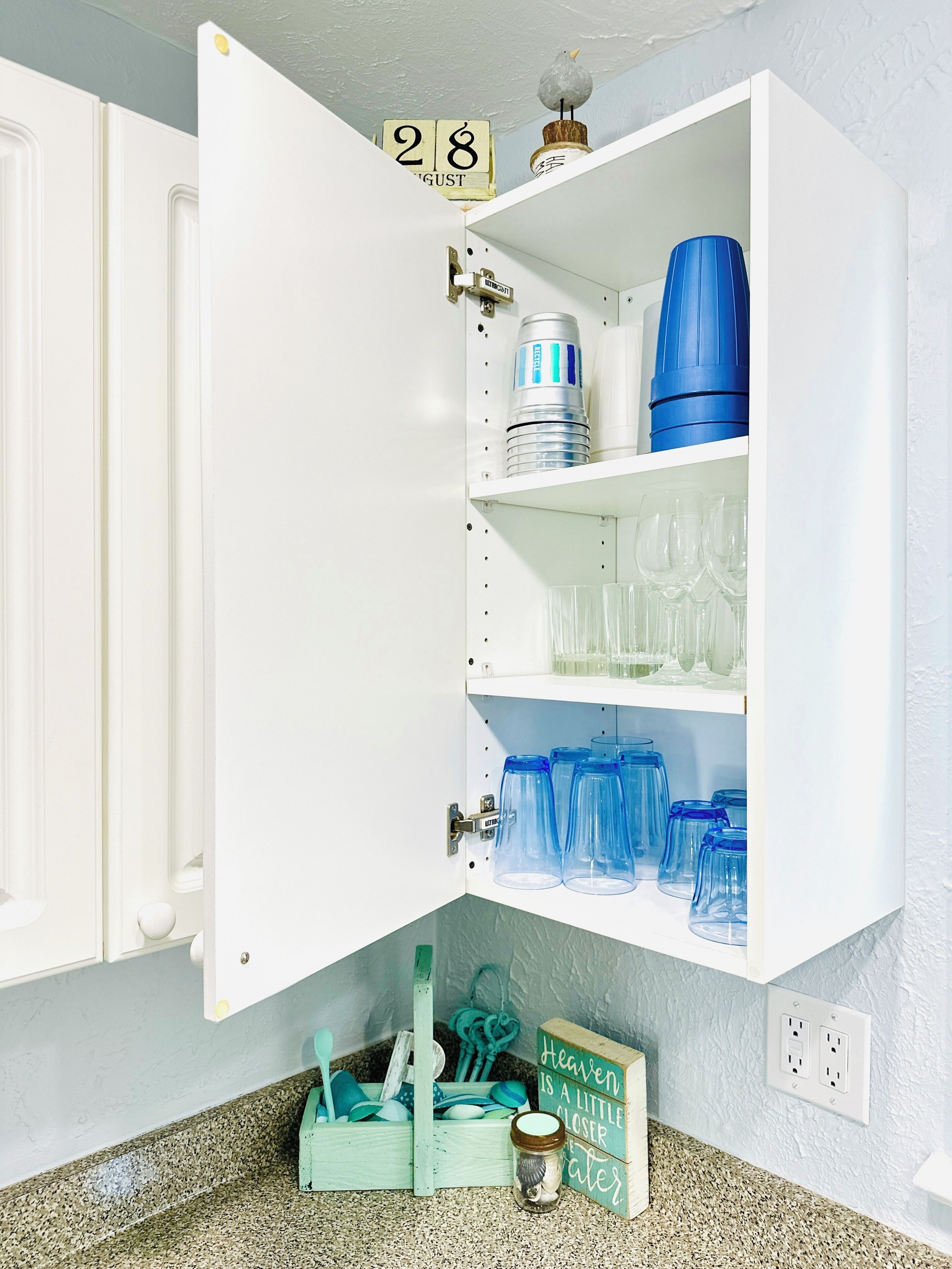 A kitchen cabinet with a date sign, a blue water dispenser, and various glassware.