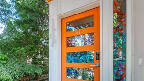 A modern house with a wooden porch, a bright orange door with stained glass panels, and a welcome mat. - Rooftop•Mural•1GB•Parking•AC•FIFAStadiums•W/D•BBQ•Mountain&Bay Views•New Kitchen (Seattle)