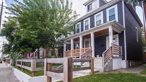 A two-story house with a covered porch and a wooden fence. - Charming 4 Bedroom Home Near Downtown Columbus with Garage Parking and Backyard. (Columbus)