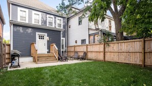 A residential backyard with a wooden deck, a lawn, and a house with a white door and windows. - Charming 4 Bedroom Home Near Downtown Columbus with Garage Parking and Backyard. (Columbus)