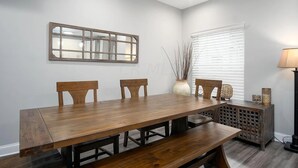 A dining room with a wooden table, three chairs, a decorative mirror, a vase with branches, and a lamp. - Charming 4 Bedroom Home Near Downtown Columbus with Garage Parking and Backyard. (Columbus)