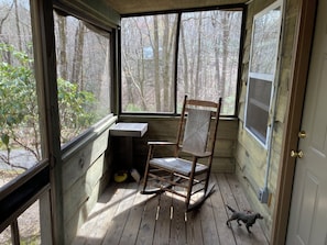 Relax in this serene corner room with a comfortable rocking chair and a view of the surrounding woods.