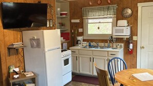 Una cocina compacta equipada con refrigerador, estufa, microondas y lavamanos. Hay un pequeño comedor con mesa y sillas.