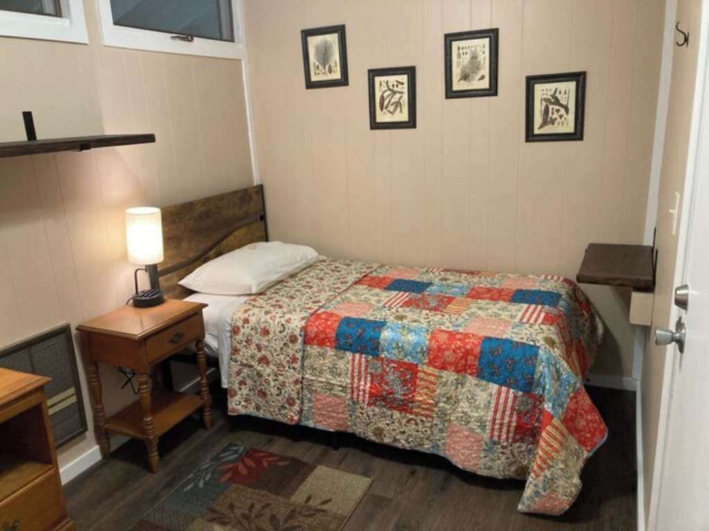 A bedroom with a bed, a nightstand, a lamp, and a wall with framed pictures.