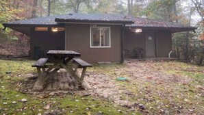 Une petite cabane avec une table de pique-nique devant, entourée d’arbres.
