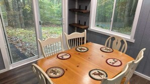 Une table à manger avec quatre chaises, entourée de fenêtres donnant sur une forêt.