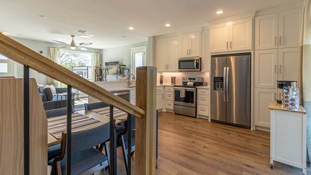 A modern kitchen with white cabinets, stainless steel appliances, and a wooden dining area.