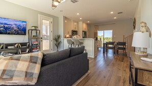 A modern living room with a grey sofa, a flat-screen TV, and a dining area with a wooden table and chairs.