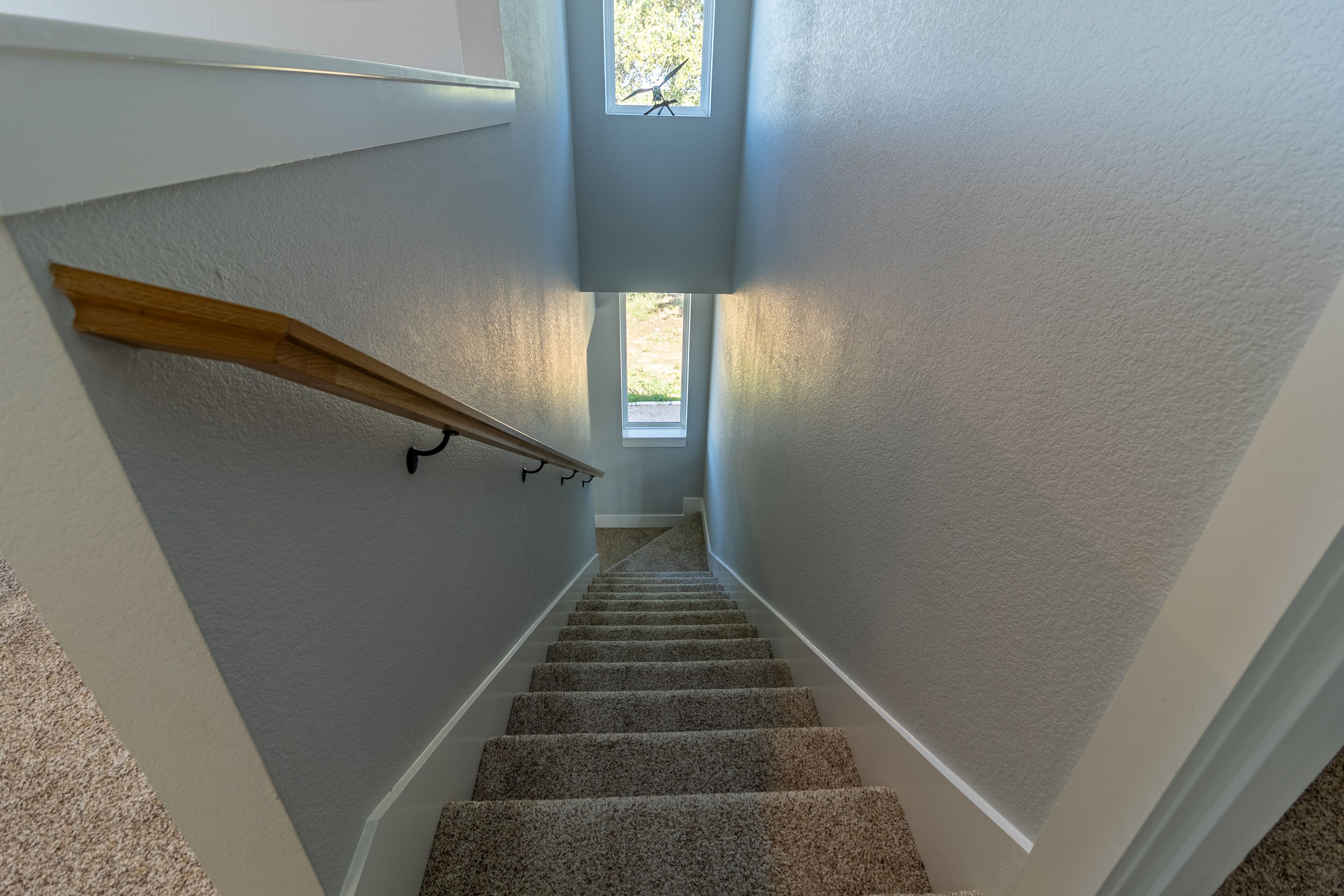 Una escalera alfombrada con barandilla de madera, paredes blancas y un pequeño ventanal en la parte superior.