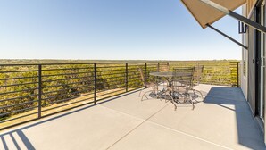 A balcony with a table and chairs, a metal railing, and a view of a green landscape.