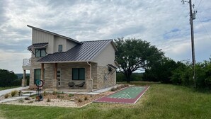 A modern two-story house with a stone facade, a sloped roof, and a front yard with a green lawn and a shuffleboard court.
