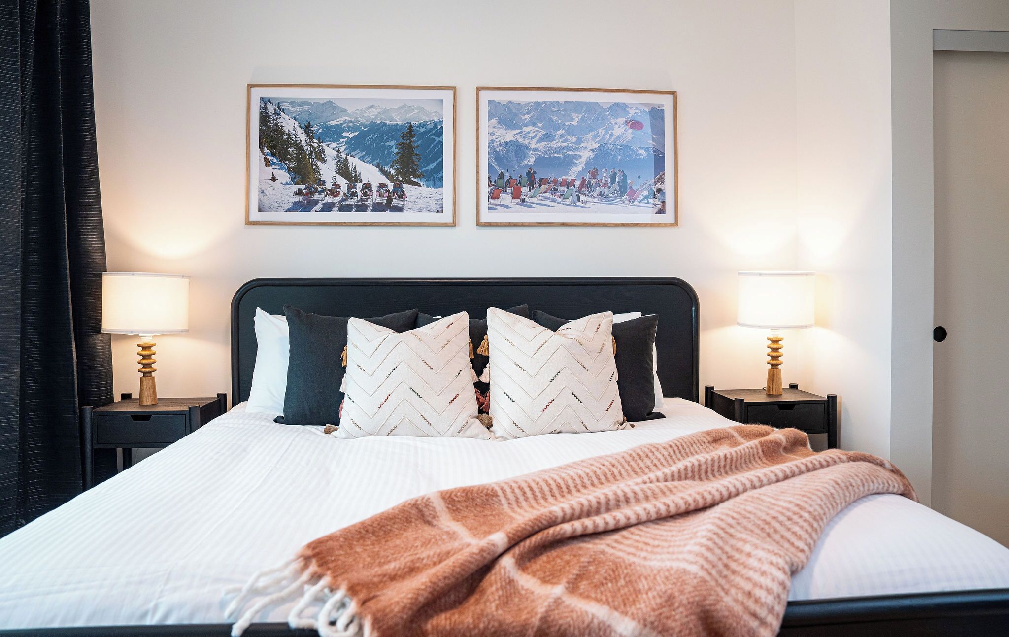 A neatly made bed with a white comforter and two pillows, flanked by two bedside tables with lamps, in a room with a simple, clean design.