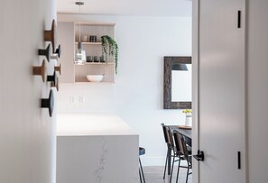 Une cuisine moderne avec un plan de travail en marbre blanc, des étagères en bois et une plante suspendue.