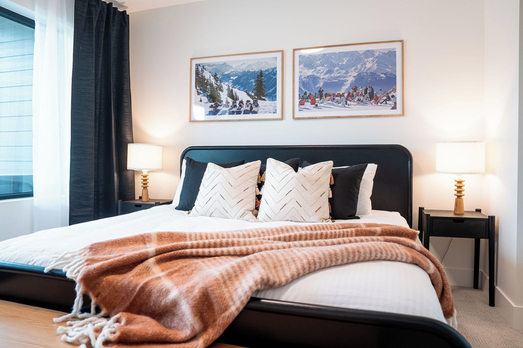 A bedroom with a bed, two bedside tables with lamps, and two framed pictures on the wall.
