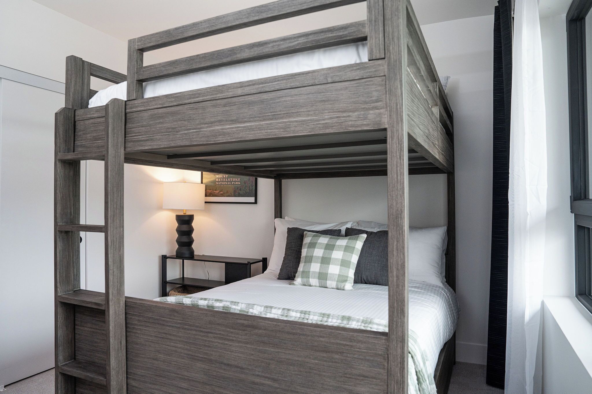 A bunk bed with a wooden frame, a bedside table with a lamp, and a framed picture on the wall.