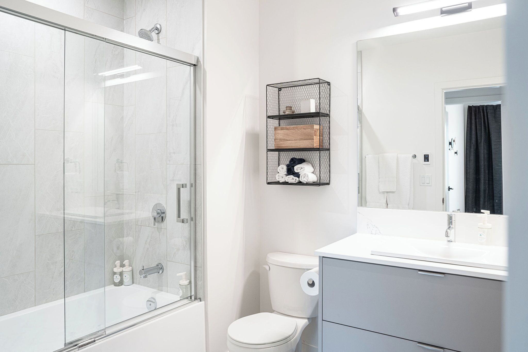 A modern bathroom with a glass-enclosed shower, a toilet, and a vanity with a mirror.