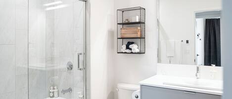 A modern bathroom with a glass-enclosed shower, a toilet, and a vanity with a mirror.