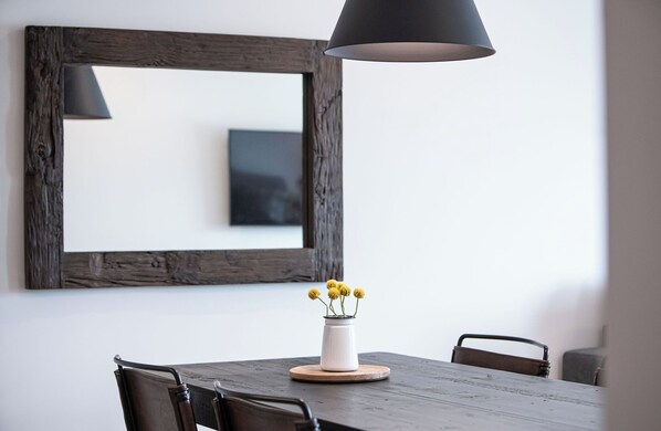 Une table à manger ornée d’un vase blanc contenant des fleurs jaunes, d’un sous-verre en bois et d’une lampe suspendue noire.