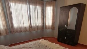 Un dormitorio con cama, cortinas, armario y una alfombra estampada.