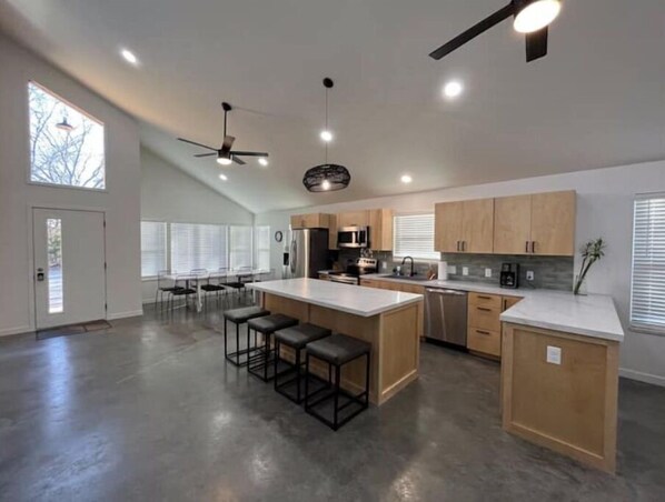 A modern kitchen with a large island, bar stools, and a ceiling fan.