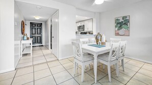 A modern kitchen with white cabinets, a microwave, and a dining area with a white table and chairs.