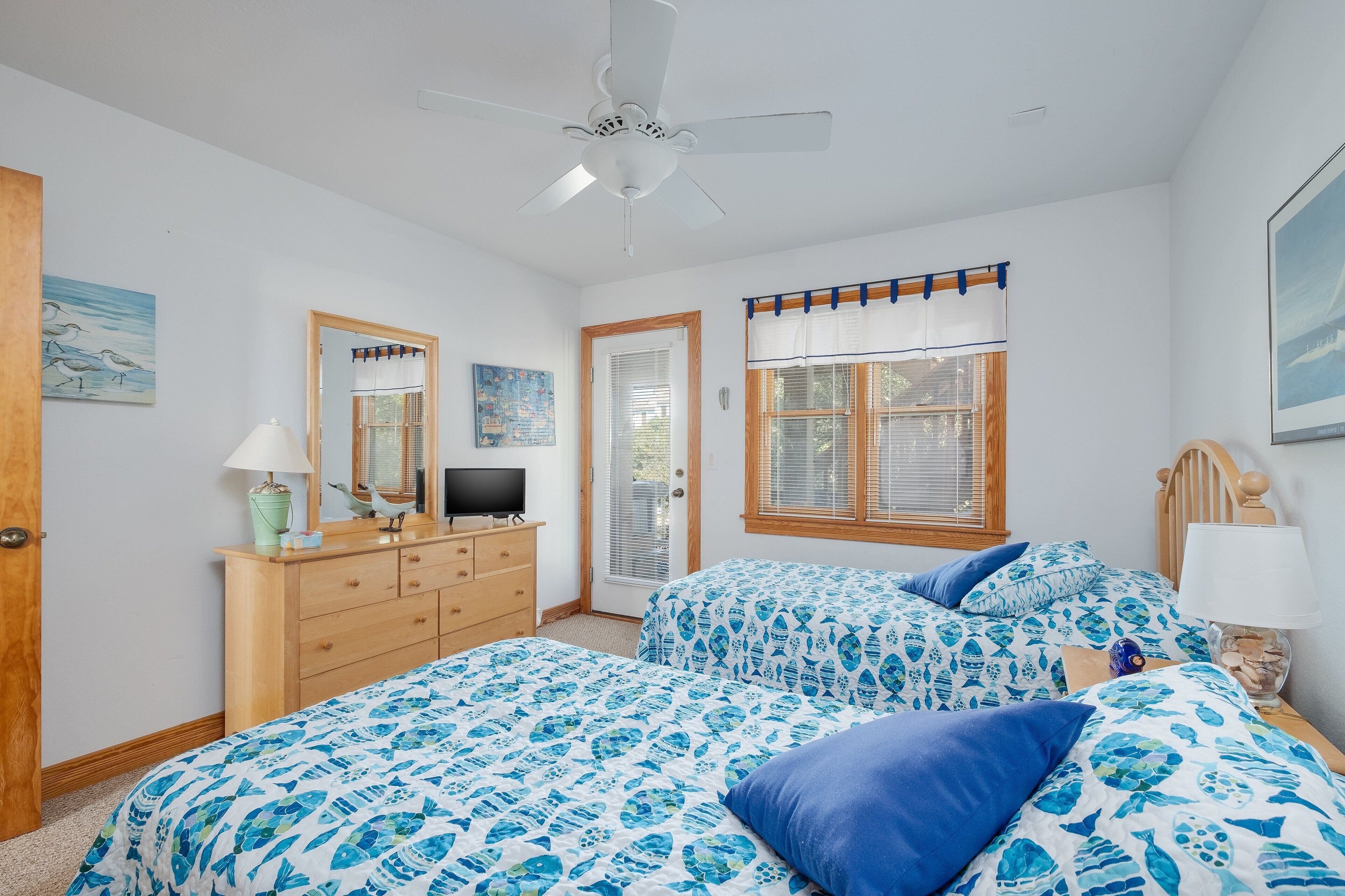 Une chambre avec deux lits, un ventilateur de plafond, une commode, un téléviseur et une fenêtre avec des stores.
