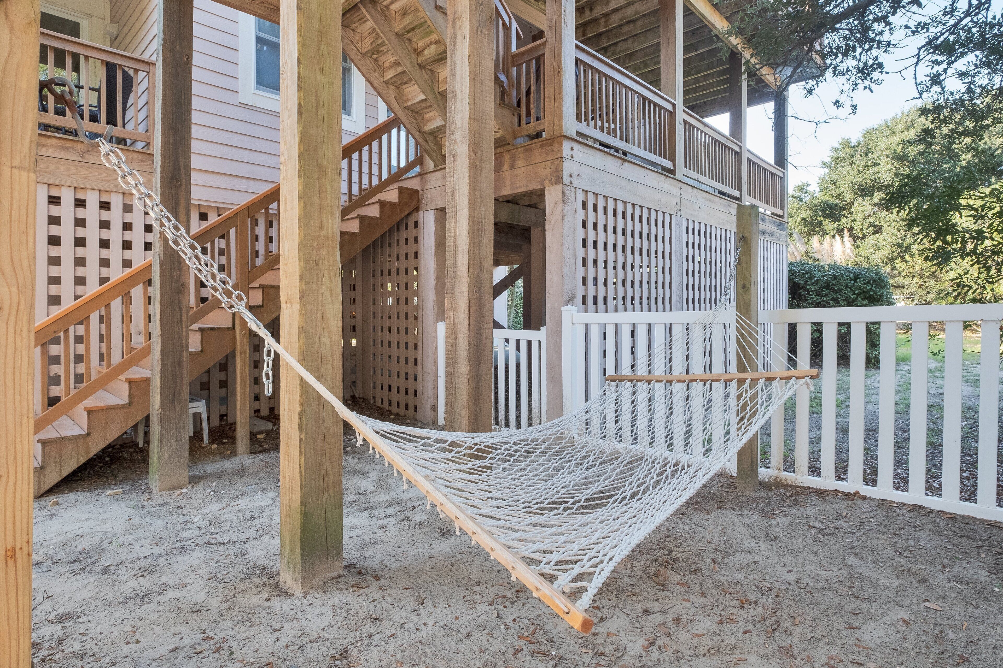 Une terrasse en bois avec une clôture blanche, un hamac et un escalier menant à un balcon.