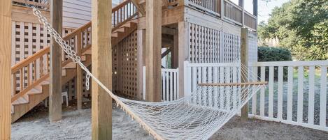 Une terrasse en bois avec une clôture blanche, un hamac et un escalier menant à un balcon.