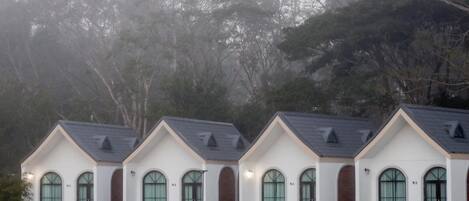 A row of identical white buildings with dark brown doors and arched windows, each with a small porch and a chair.