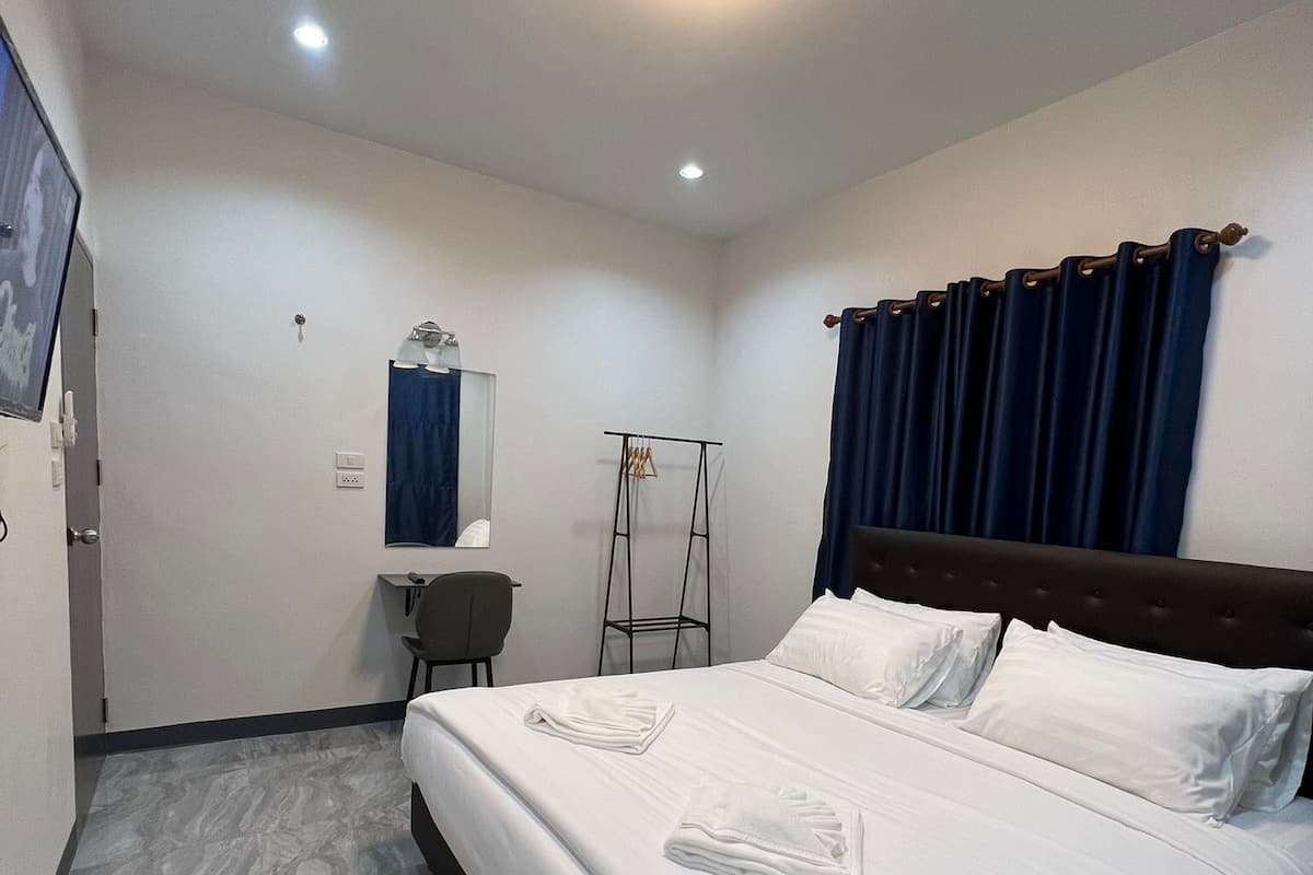 A hotel room with a large bed, a small desk, a chair, a mirror, and a window with curtains.