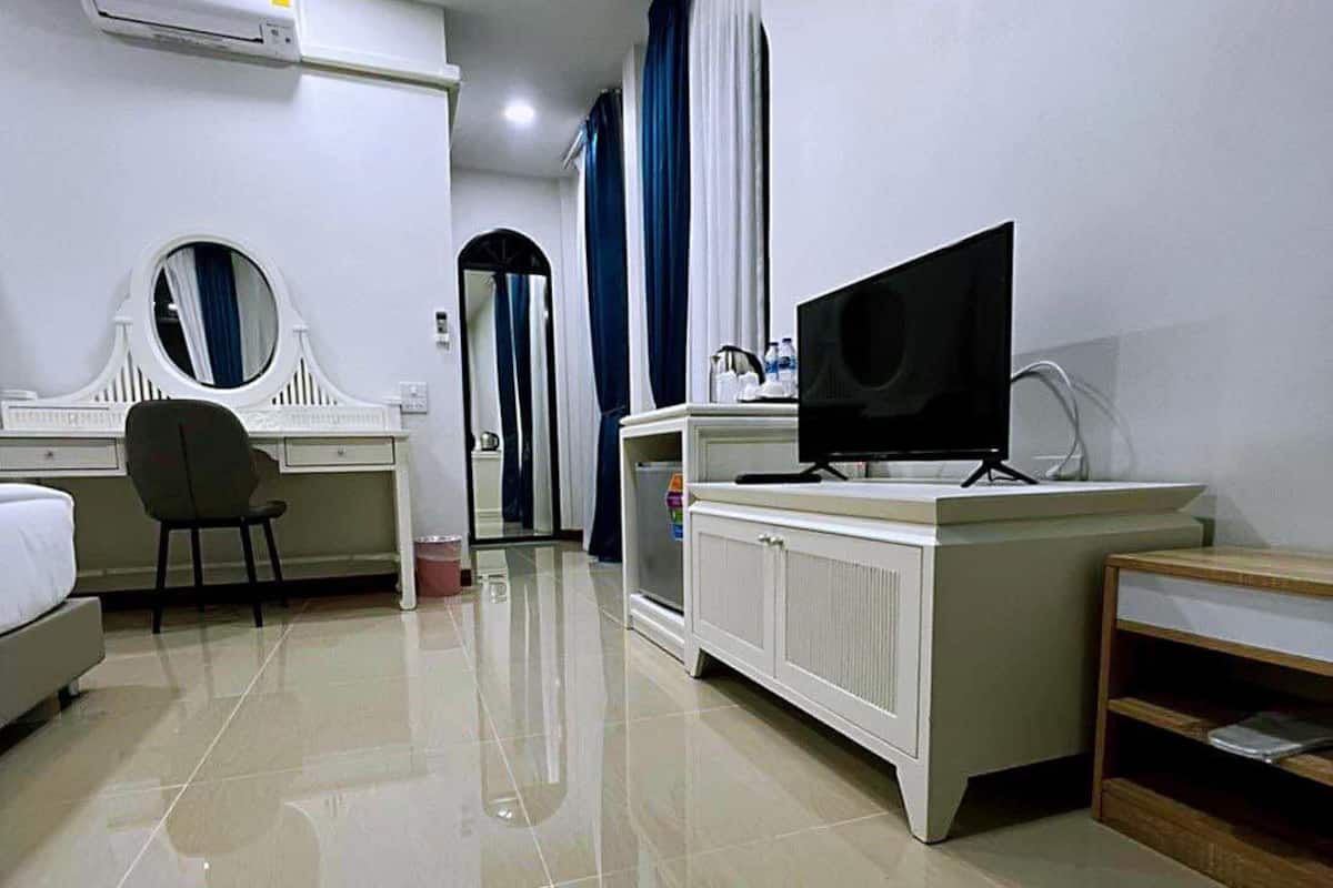 A hotel room with a bed, a desk with a chair, a television, an air conditioning unit, and a mirror.